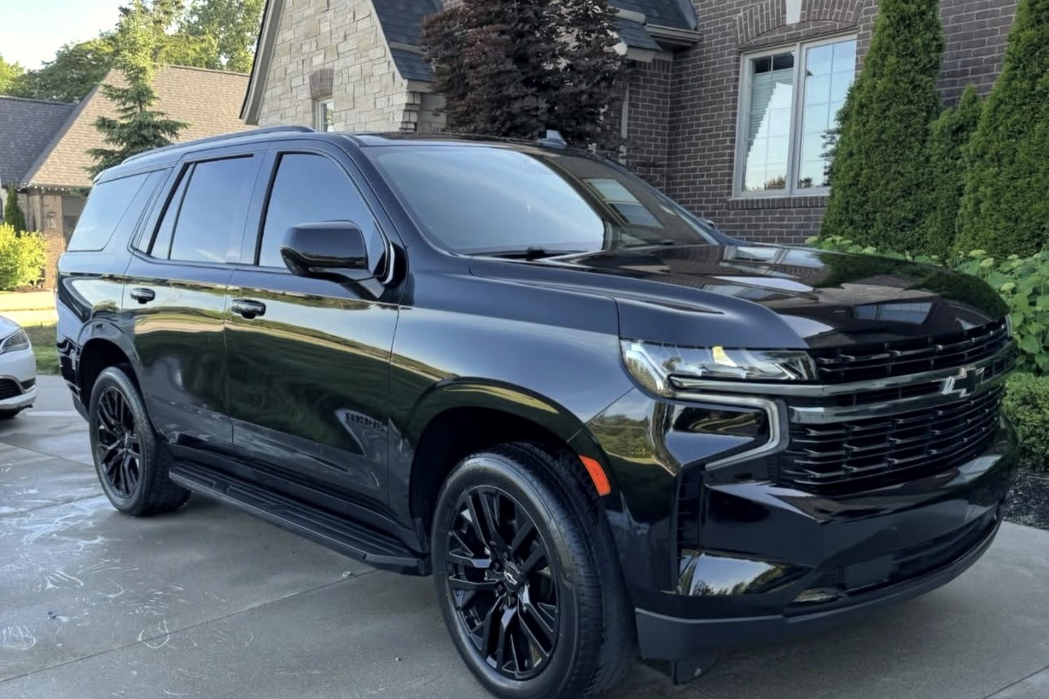 A black Chevrolet Tahoe after detailing, paint glossy and reflecting the house behind it