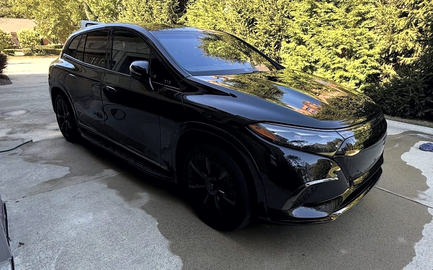 Black Mercedes-Maybach EQS SUV on a driveway, its bodywork reflecting the trees overhead after a full detail